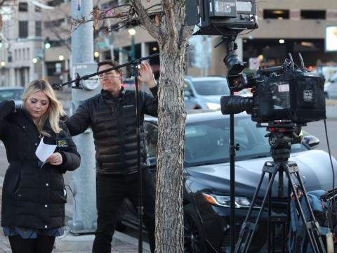 A television reporter speaks beside a camera operator on a city street.