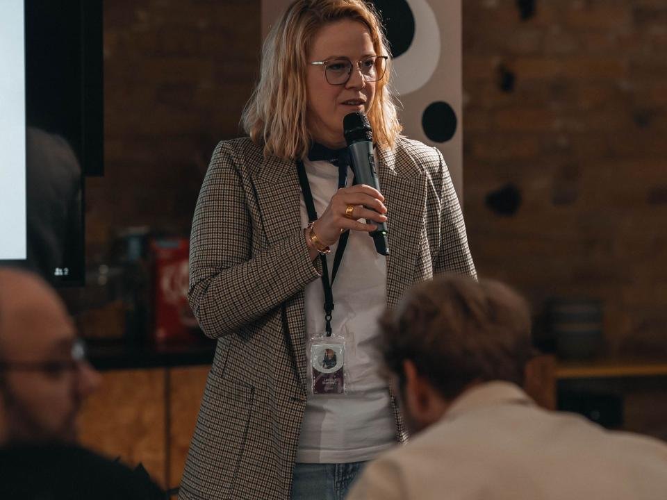 A woman speaks into a microphone during an indoor community event.