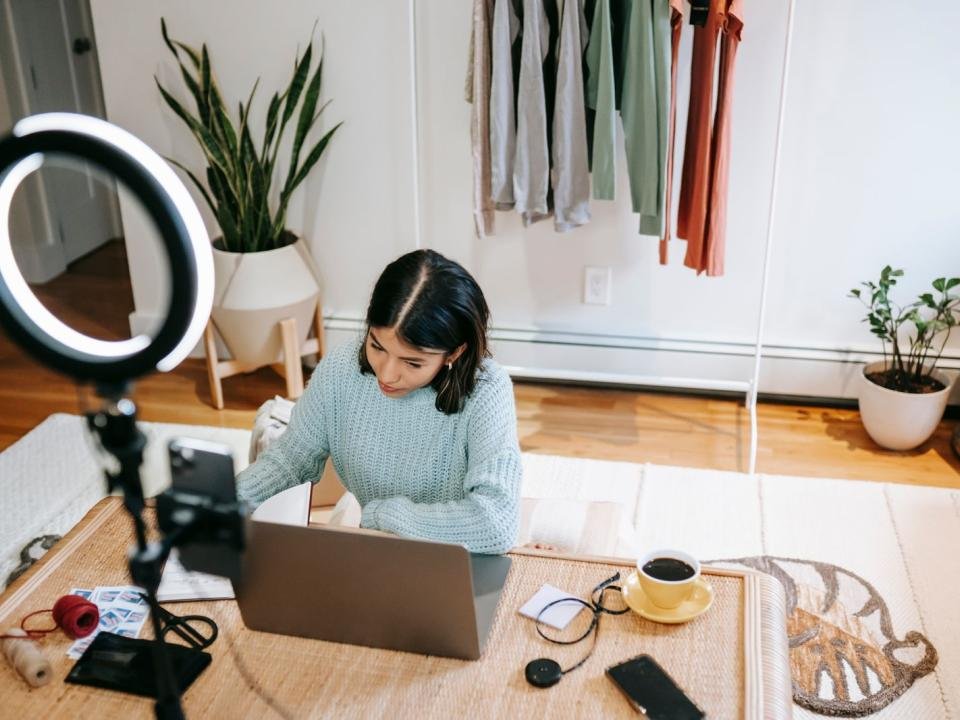 A woman works at a laptop in a home studio with creative equipment nearby.