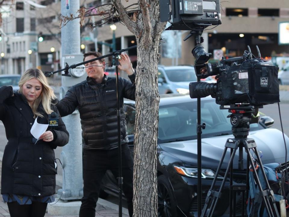 A television reporter speaks beside a camera operator on a city street.